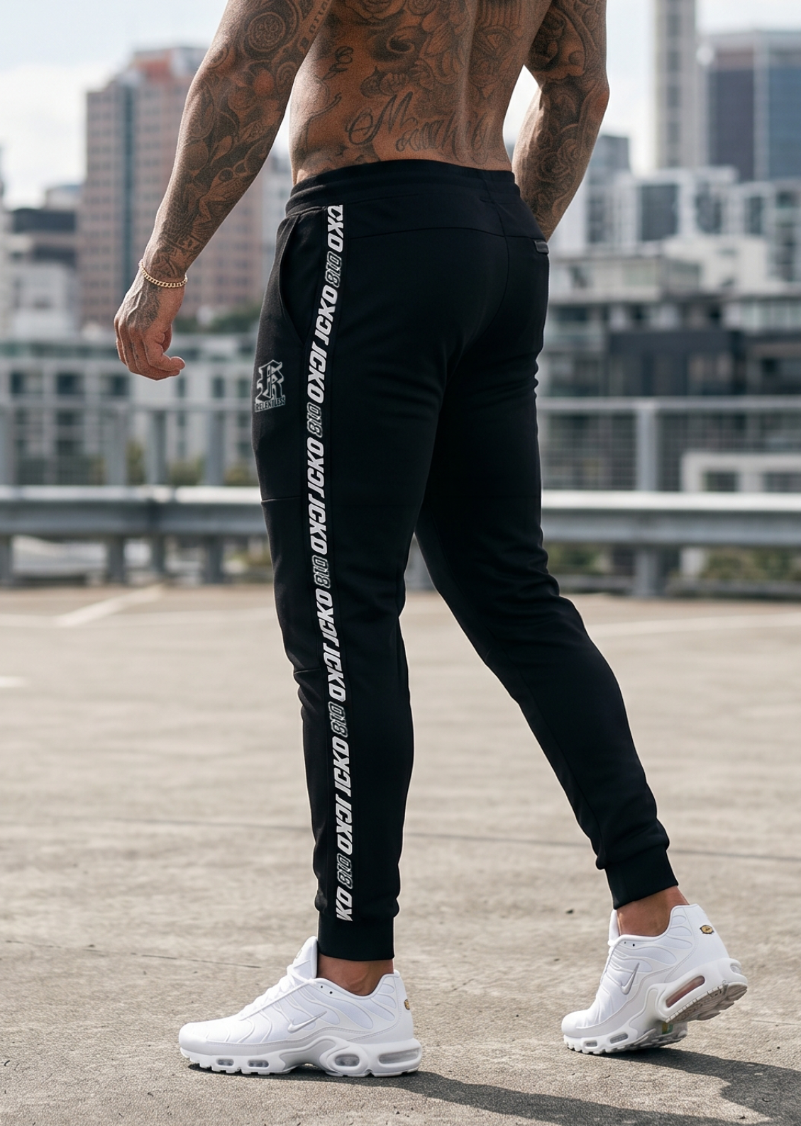Person wearing black jogger pants with white text and white sneakers in an urban setting