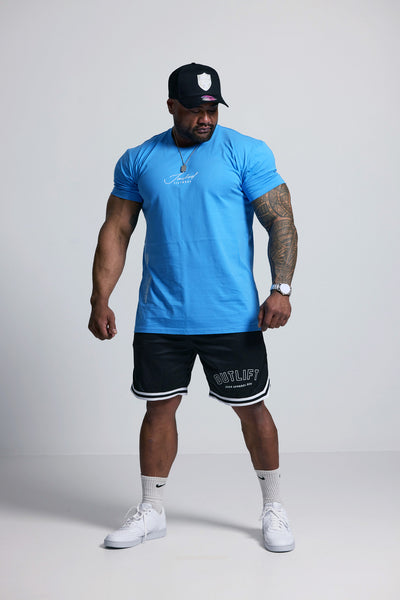 Man wearing a blue t-shirt, black shorts, and white sneakers on a plain background