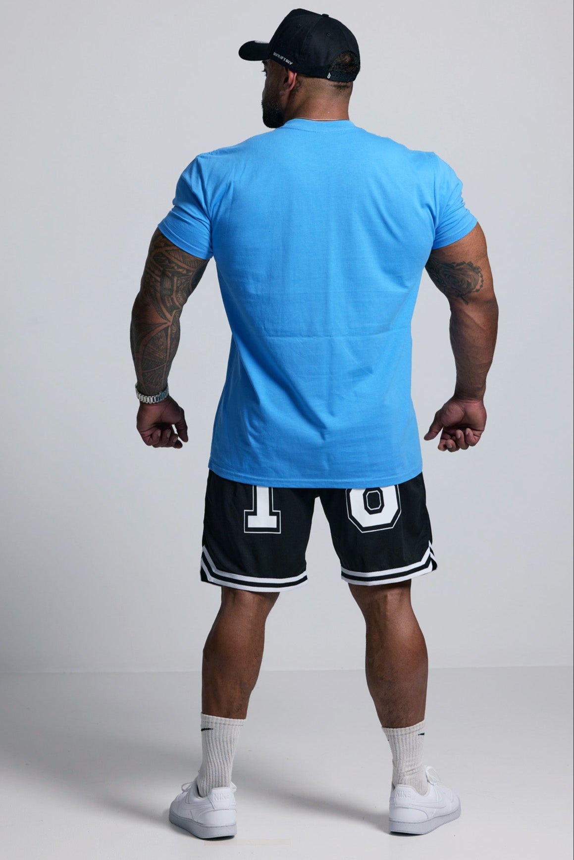 Person wearing a blue t-shirt and black shorts with white accents on a plain background