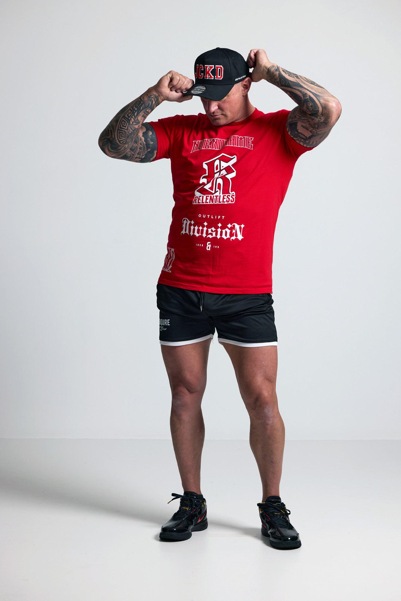 Person wearing a red t-shirt and black shorts with tattoos, posing against a white background