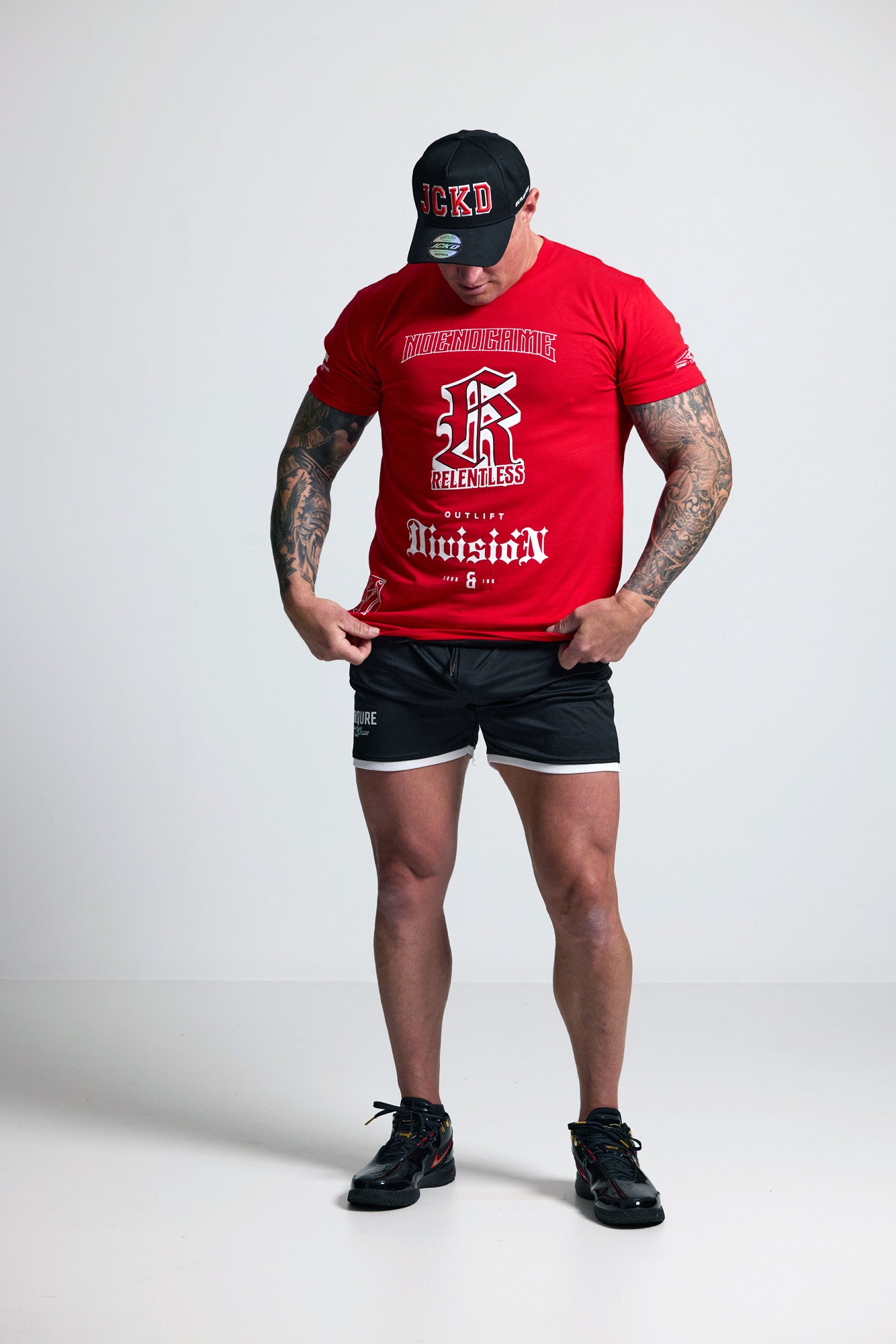 Person wearing a red t-shirt with branding and black shorts on a white background
