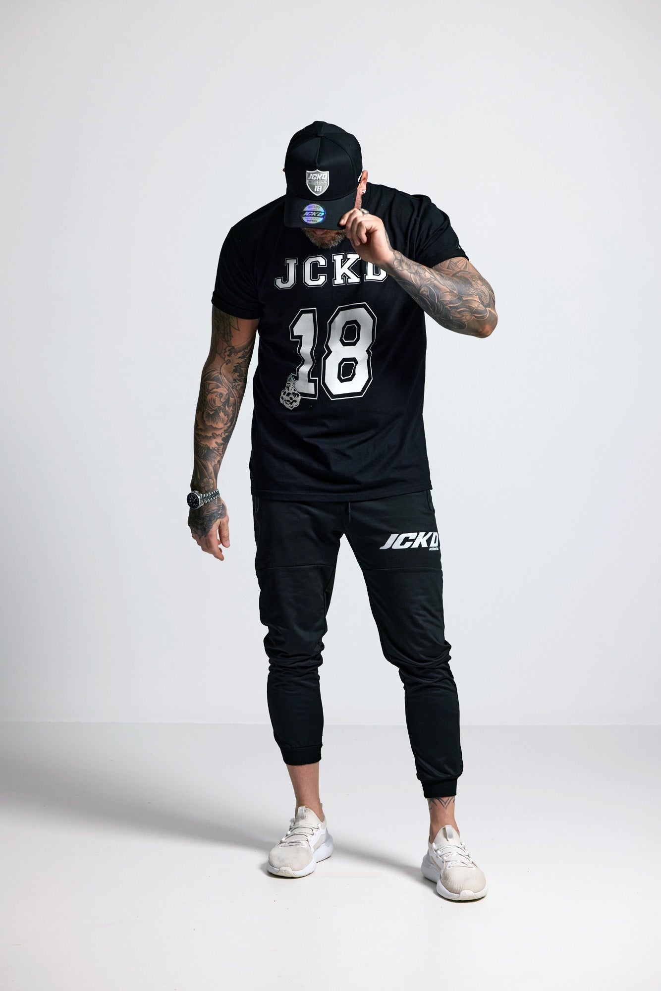 Person wearing a black t-shirt with 'JCKD' branding and black pants on a white background