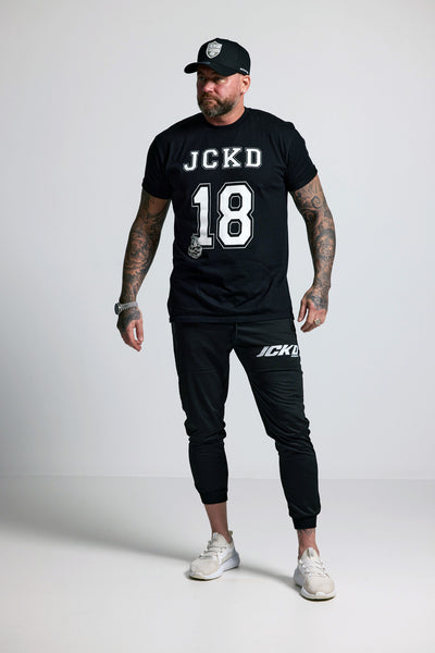 Person wearing black t-shirt and pants with 'JCKD' branding on a white background
