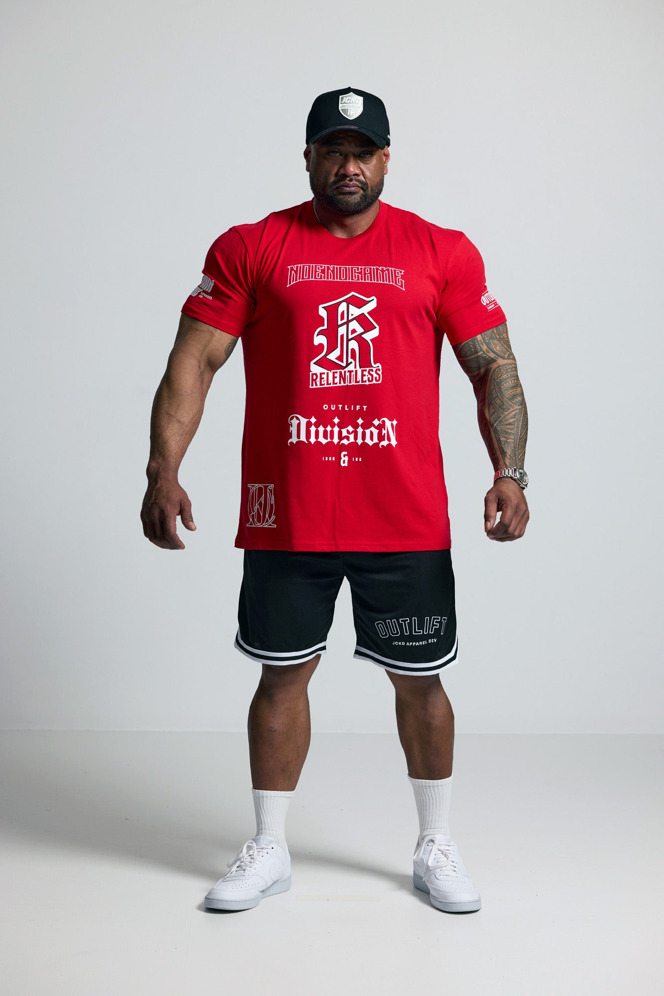Man wearing a red t-shirt and black shorts with visible branding on a white background