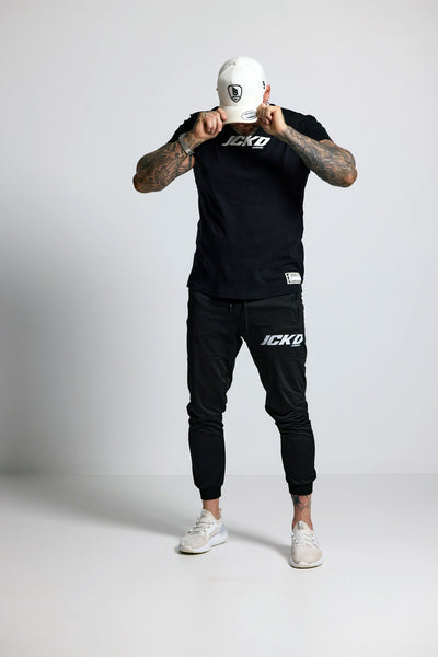 Person wearing black JCKD branded outfit with white cap on a light gray background
