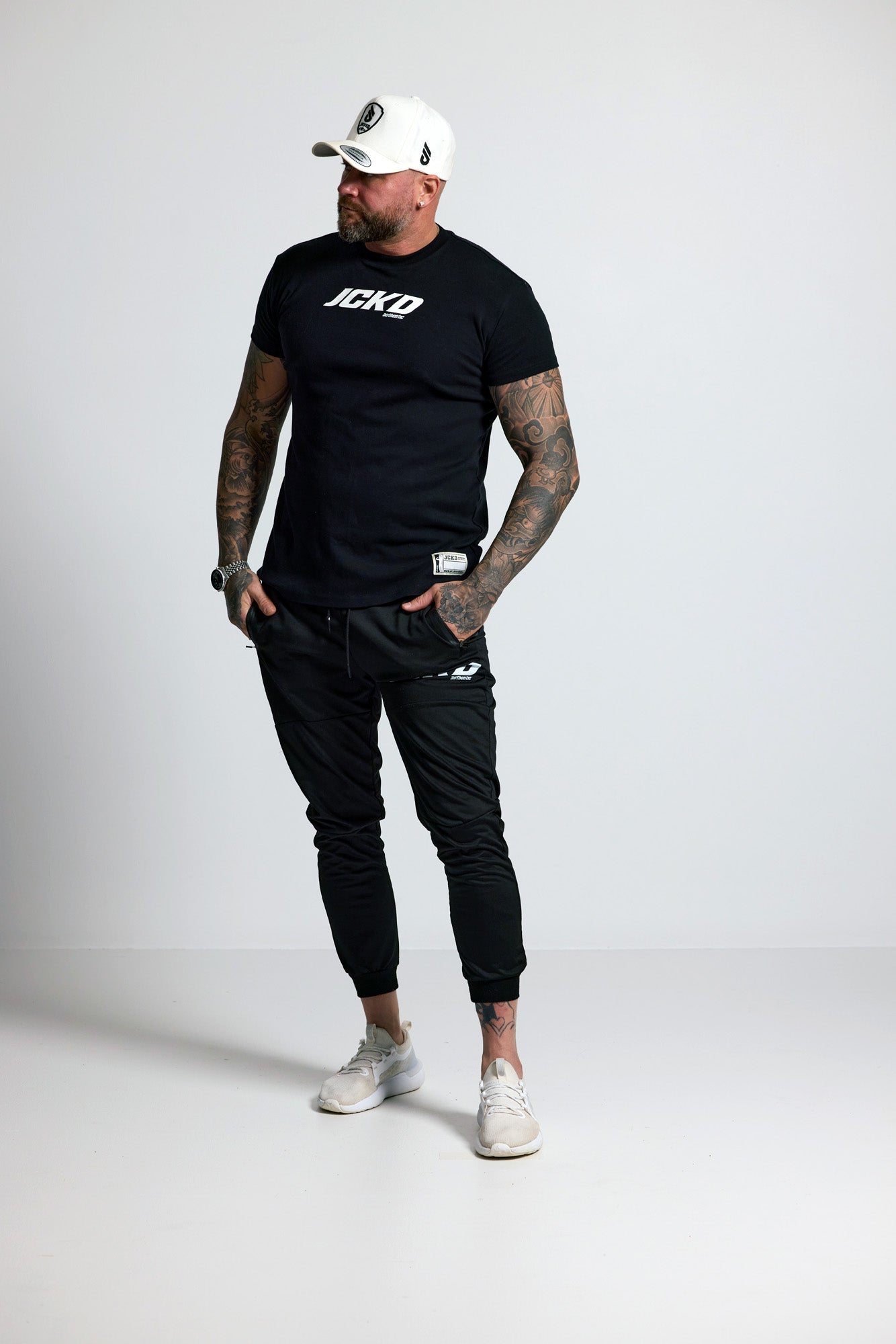 Man wearing a black t-shirt with 'ICE' logo, black pants, and white sneakers on a white background