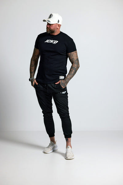 Man wearing a black t-shirt with 'ICE' logo, black pants, and white sneakers on a white background