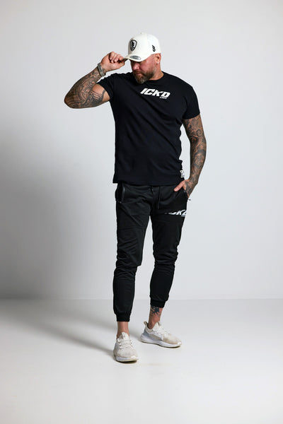 Man wearing a black t-shirt and pants with visible branding on a white background
