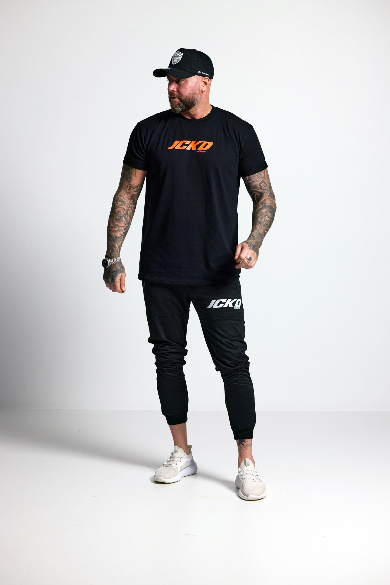 Man wearing a black t-shirt and jogger pants with 'JCKD' branding on a white background