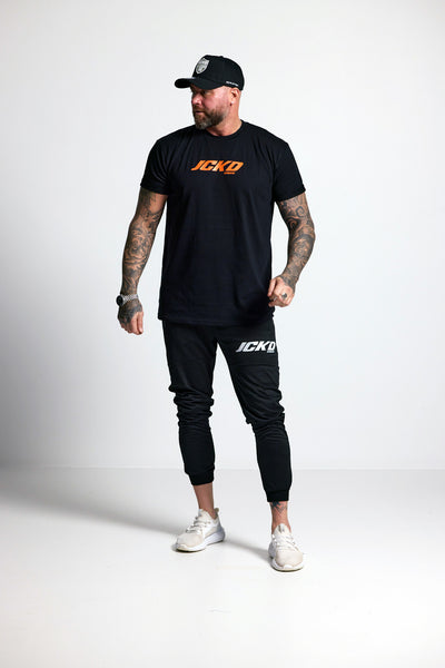 Man wearing a black t-shirt and jogger pants with 'JCKD' branding on a white background