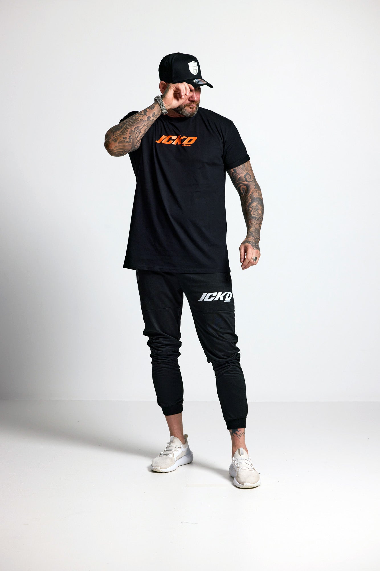 Person wearing a black t-shirt and jogger pants with 'JCKD' branding on a white background