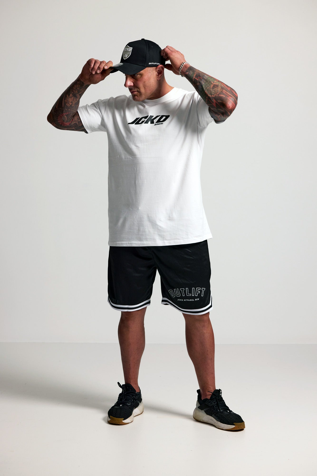 Person wearing a white t-shirt with black text and black shorts with white text, standing against a plain background.