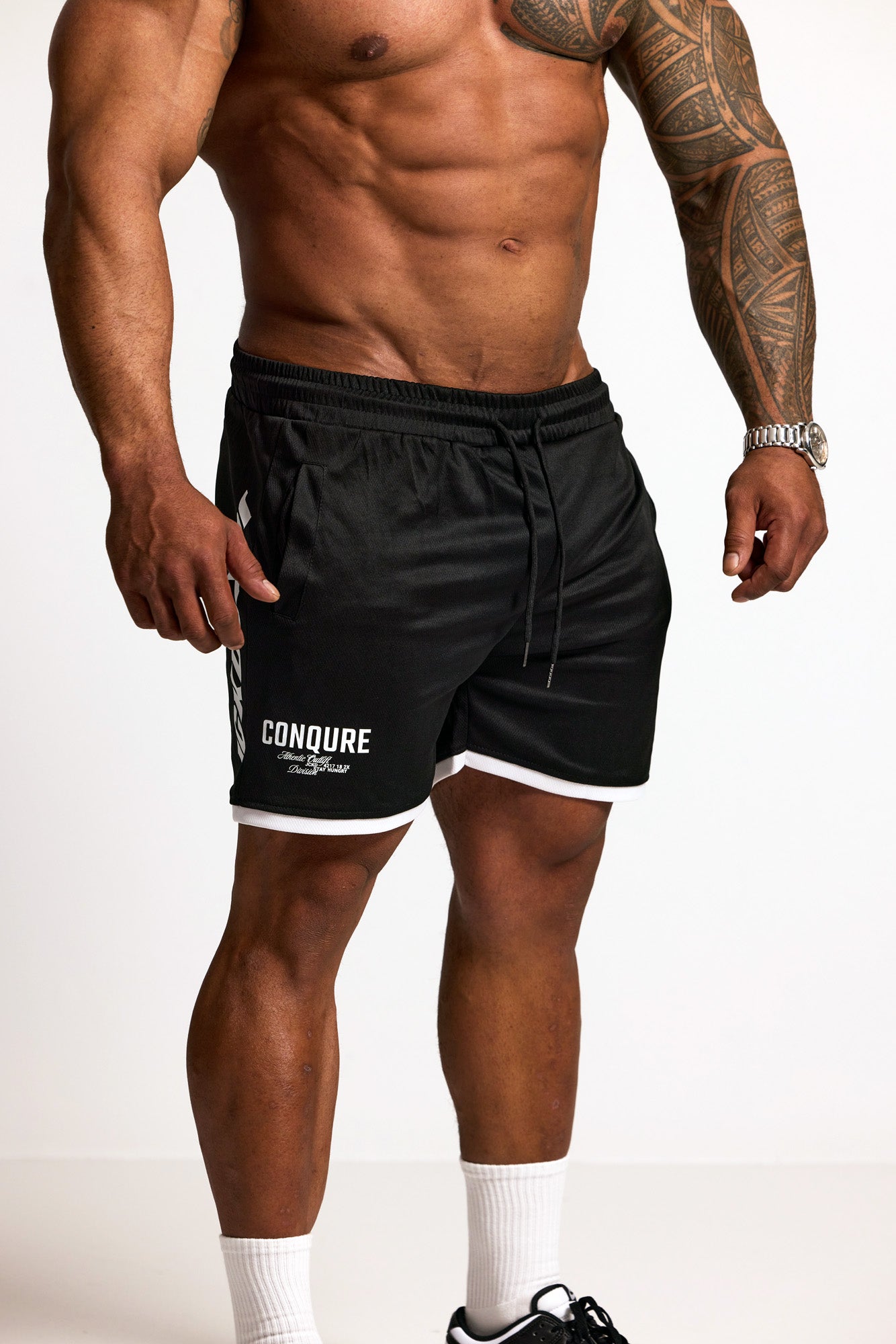 Person wearing black athletic shorts with 'Conquer' branding on a white background