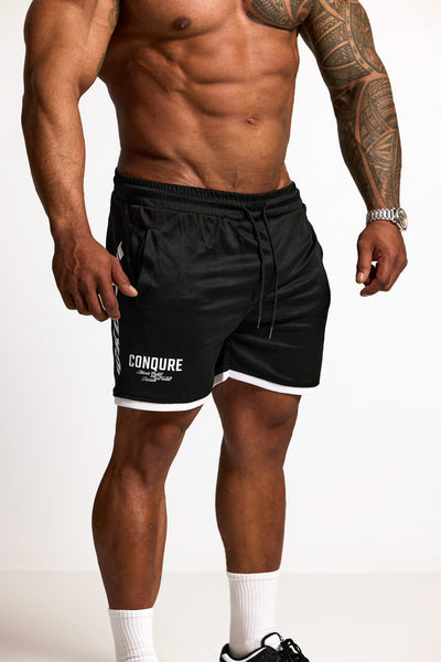 Person wearing black athletic shorts with 'Conquer' branding on a white background