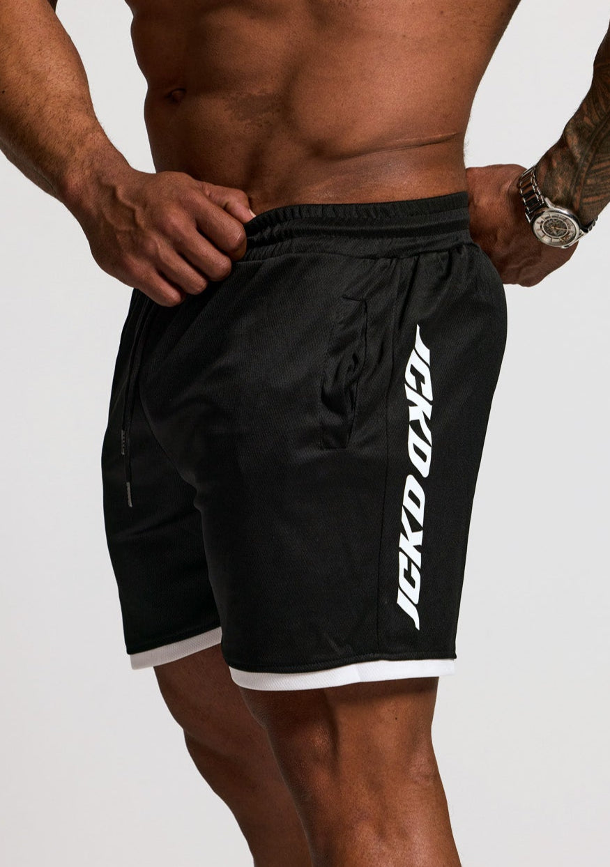 Person wearing black shorts with a brand logo on a plain background